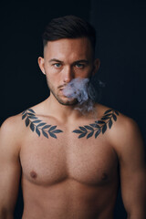 Fototapeta premium Modelling snapshots. Pensive serious tanned attractive handsome naked man thinking looks at camera to you smoking posing isolated in black studio background. Fashion offer. Copy space for ad. Closeup