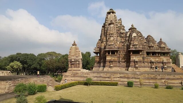 A sweeping wide-angle captures Khajuraho&rsquo;s majestic temple, with ornate stone carvings, towering shikharas, and regal design, surrounded by manicured green gardens that enhance its timeless beauty and