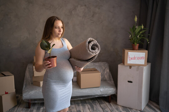Pregnant woman alone in new apartment, standing in front of boxes during moving in new home, housing program for mothers