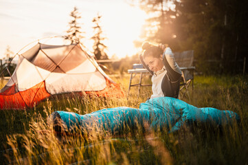 Woman relaxing and lie in a sleeping bag in the tent. Sunset camping in forest. Mountains landscape...