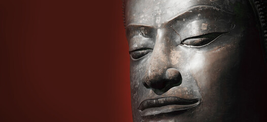 The head of an ancient Buddha statue was made of bronze. image on copy space classic red background.