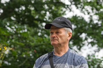 Naklejka na ściany i meble Portrait of serious caucasian senior man with black baseball cap and casual clothing. Isolated on the nature background.