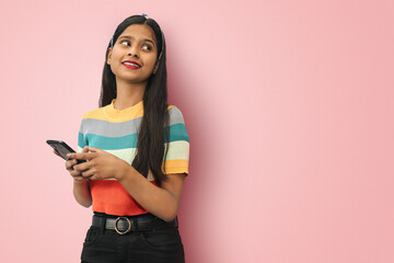 Photo of cheerful cute gorgeous attractive indian asian girl holding telephone with hands smiling toothily and looking to other side with mock up space to write text