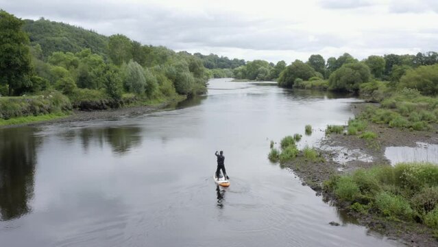 Lone man paddles SUP on small peaceful river in rural countryside
