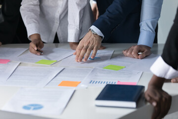 Meeting table and hands of multiethnic business colleagues close up. Team of businesspeople discussing paper reports with sticky notes, analyzing marketing, statistic data, working on project together