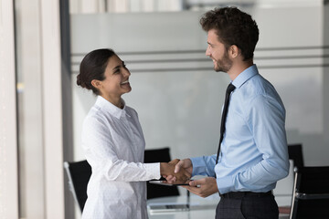 Two happy confident diverse business people shaking hands in office, smiling, laughing, talking. Customer giving handshake to manager, lawyer, ending meeting, negotiation, deal