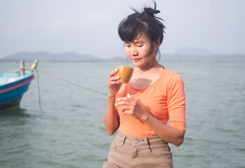 Woman holding hot coffee.  with blur river water sea background.tourist travel tropical summer in holidays.relax vacation with nature ocean.morning hot drink espresso snack breakfast in cafe resort.