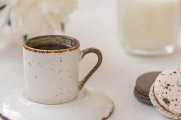 White and chocolate creamy macarons, coffee or tea, white peony, candle on white background. Freshness concept. Traditional French dessert for coffee.