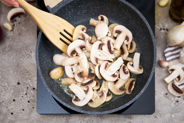 Sliced mushrooms in a frying pan on induction hob at domestic kitchen