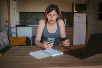 young asian woman at home, remote work at laptop. shopping online at home, lady is holding credit card and using smartphone and computer.