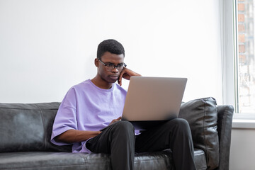 Black man with laptop sitting on couch, pensive look - obrazy, fototapety, plakaty