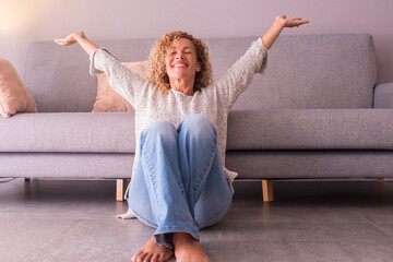 Happy and satisfied woman at home sitting on the floor opening arms and smiling. Concept of joyful lifestyle female people. Indoor leisure activity, Success and enjoying lifestyle. Indoor apartment - obrazy, fototapety, plakaty