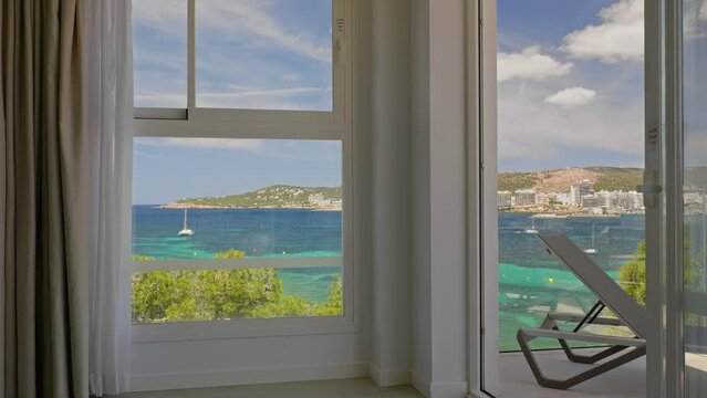 Tropical sea bay view through the window of a hotel room with balcony and sunbed. Relax and vacation concept.