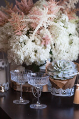 A bouquet of white hydrangeas and pink astilba, succulent, candles and a fashionable glass for dessert and champagne with wine inside. Cozy interior. The concept of a party, wedding and holiday.