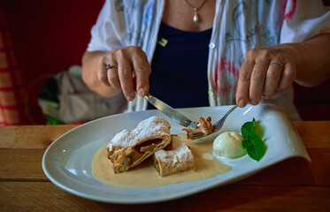 Woman eats a fresh apple strudel pie served with vanilla souse and  ice cream on a white ceramic plate