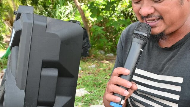 an indonesian man is doing karaoke alone on the beach using a mic and portable speakers