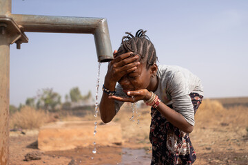 Little African girl cooling her forehead and face on a scorching hot day at the village water point