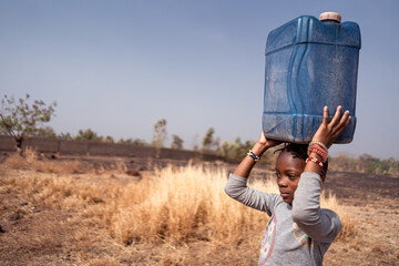 Close up of a serious young African girl carrying a blue water canister on her head