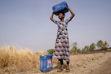 Young African girl with water containers looking into the distance, estimating the long walk to the...