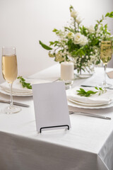 Mockup white blank space card for table number or menu. Wedding teble decoration with white flowers, glasses and white napkins. Elegantly decorated table at a wedding reception. 