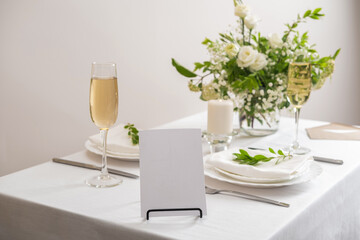 Mockup white blank space card for table number or menu. Wedding teble decoration with white flowers, glasses and white napkins. Elegantly decorated table at a wedding reception. 