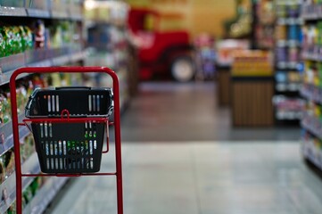 Shopping goods with red shopping cart and black basket near the shelf in supermarket 