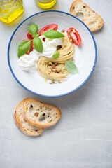 Plate of spaghetti with stracciatella di bufala, pistachios and green basil, top view on a light-grey stone background, vertical shot with space