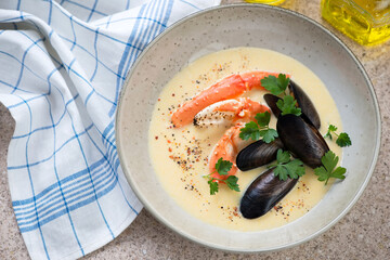 Plate of seafood soup with crab claws, mussels and fresh parsley, high angle view on a beige marble background