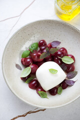 Plate with mozzarella cheese, slices of sweet cherry and fresh basil, vertical shot on a beige marble background, middle close-up, elevated view
