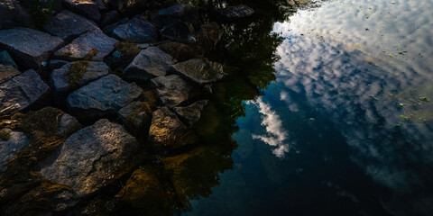 Fototapeta premium Abstract geometry of riverbank rocks and cloud reflections in the water at Big Stone Lake animal sanctuary in Minnesota, USA.