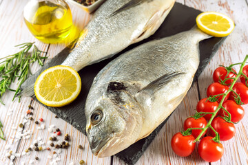 Fresh fish dorado and ingredients for cooking. Raw fish dorada with spices and herbs on gray concrete table. Seafood, restaurant, diet, healthy food background. 