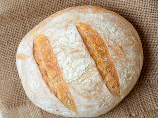 A close-up of freshly baked wheat bread with a crispy crust lies on a linen cloth. Top view flat lay
