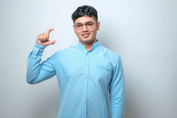 Fototapeta premium Young handsome man smiling and confident gesturing with hand doing small size sign with fingers looking and the camera. measure concept.