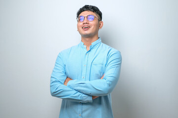 Portrait of young handsome Asian man wearing casual shirt and glasses standing with arms crossed and smiling at camera