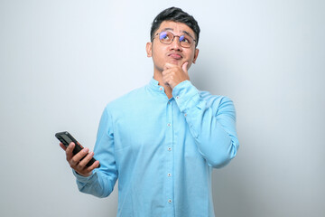 Young Asian man using mobile phone thinking and looking up while hand on chin