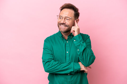 Middle age caucasian man isolated on pink background thinking an idea while looking up