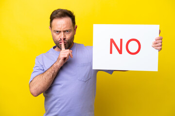Middle age caucasian man isolated on yellow background holding a placard with text NO doing silence...