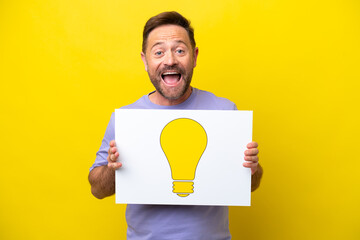 Middle age caucasian man isolated on yellow background holding a placard with bulb icon with happy expression