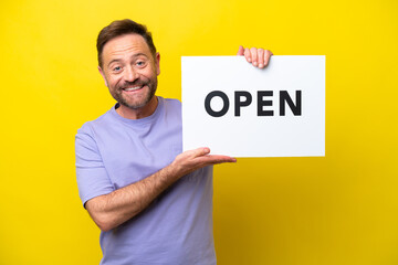 Middle age caucasian man isolated on yellow background holding a placard with text OPEN with happy expression