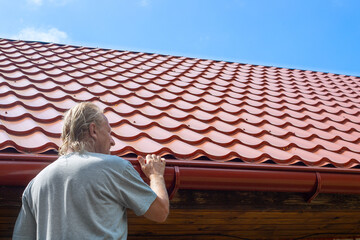 A man inspects a gutter on a roof drainpipe. Drainage of rainwater from the roof
