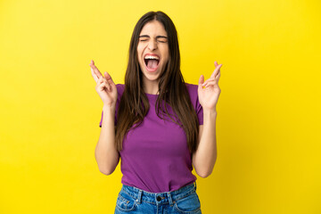 Young caucasian woman isolated on yellow background with fingers crossing