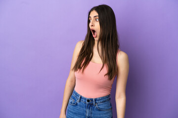 Young caucasian woman isolated on purple background doing surprise gesture while looking to the side