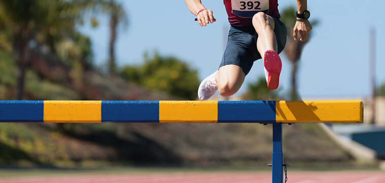 Athlete running a hurdle race in a stadium, runner jumping over a hurdle during track and field event