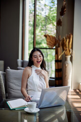 Young beautiful asian woman having a video call using a laptop and laughing, sitting in office, cafe or coworking space. Conference call, working online or blogging