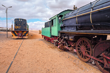 Old unused steam and diesel locomotive train at Wadi Rum train station, sandy desert around