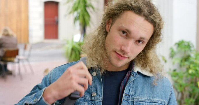 Portrait of a handsome male student with bag in a college cafeteria. Face of retro hunk with blonde hair and a positive attitude. Trendy guy feeling relaxed and looking confident while at the mall