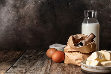 Baking ingredients: milk, flour, butter and eggs on wooden background. Dark key, rustic style, copy...