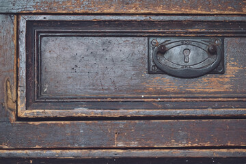 wooden drawer of an aged vintage dresser with a rustic metal handle and a keyhole as a background