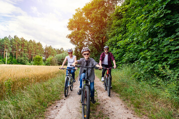 Cheerful young family cycling in meadow at hot sunny day