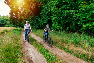mather and her son cycling in summer in the park on bicycles